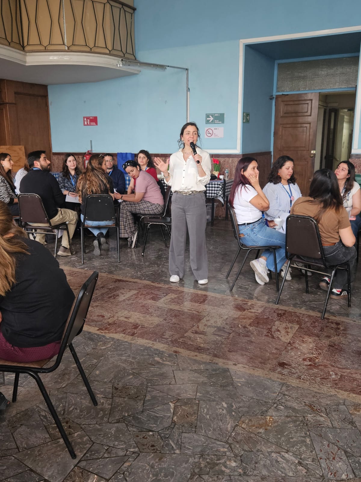 Cecilia María Aguirre facilitando un taller, micrófono en mano, junto a un equipo