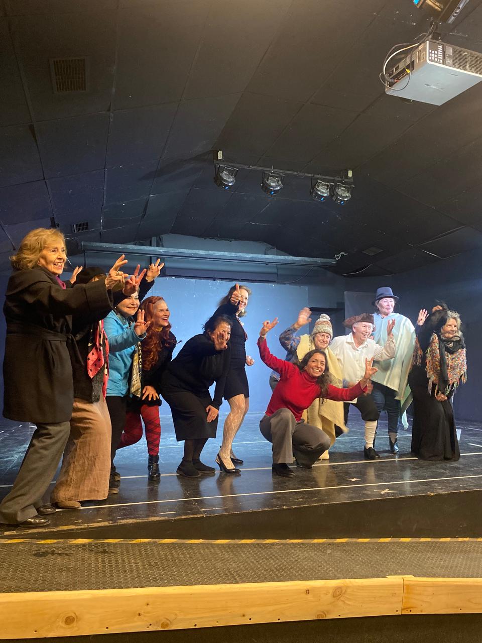 Grupo de participantes saludando con los brazos en alto sobre un escenario de teatro